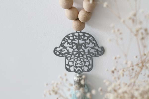 Decorative Hamsa wall hanging with wood bead accents, featuring intricate patterns and a natural, rustic aesthetic, ideal for adding a touch of cultural charm and spiritual significance to your home decor