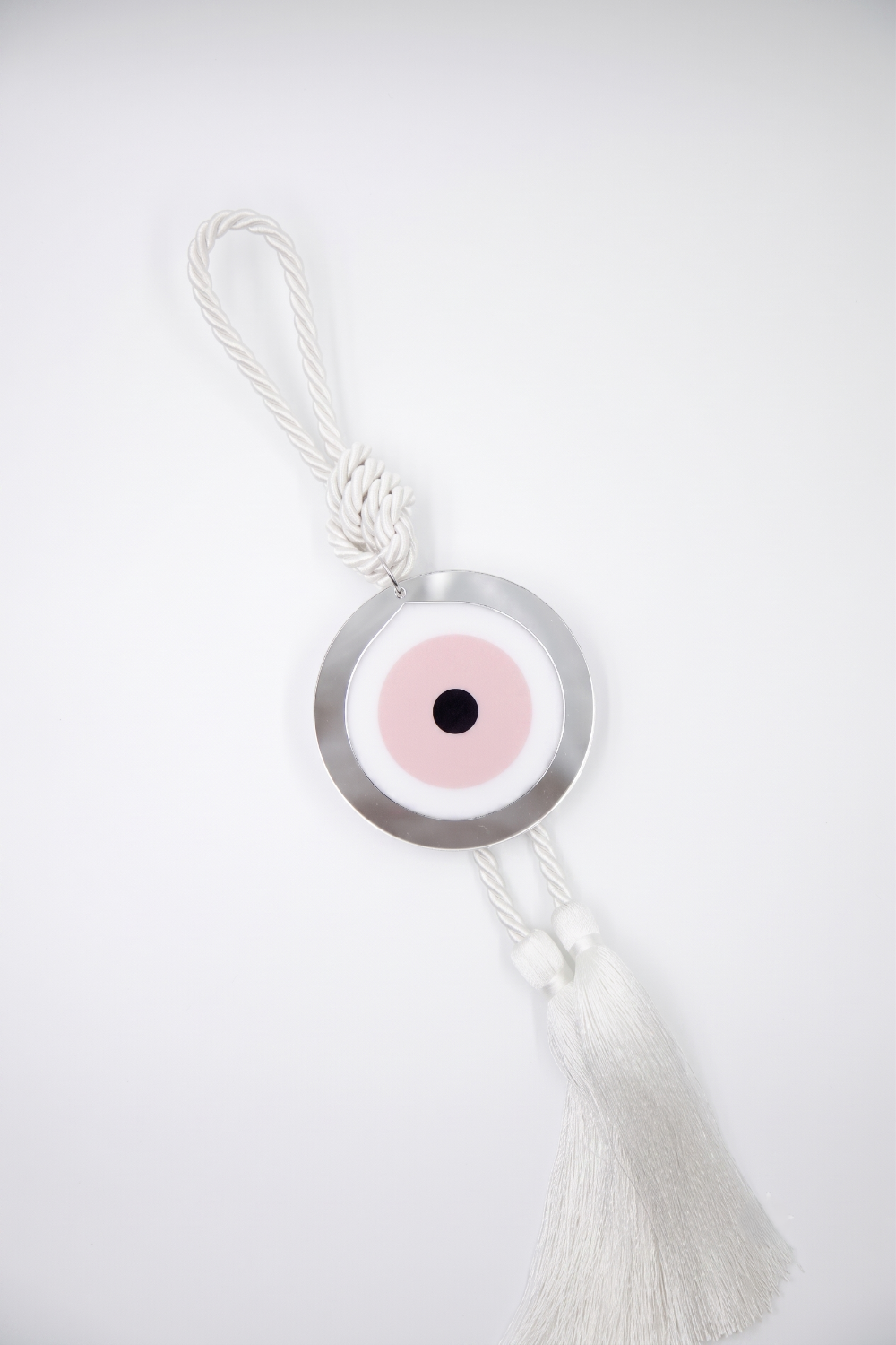 A silver-toned evil eye hanging ornament with a white tassel, featuring a pink and black eye motif on a white background.